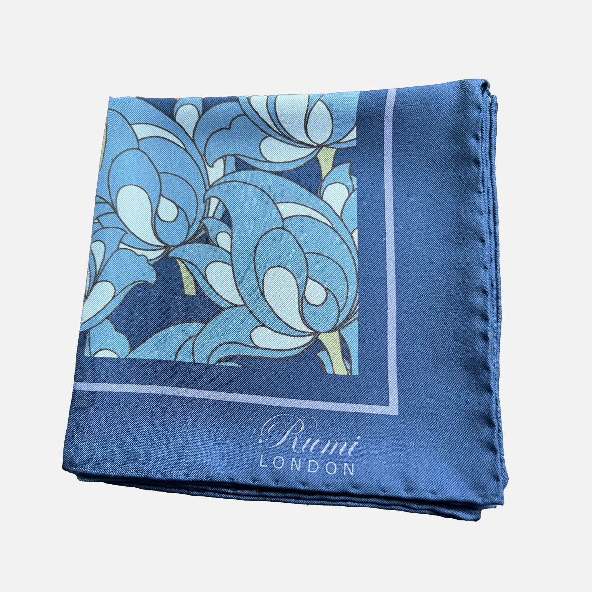 Folded square silk scarf with blue florals on a blue background and border and 'Rumi London' branding in a corner.