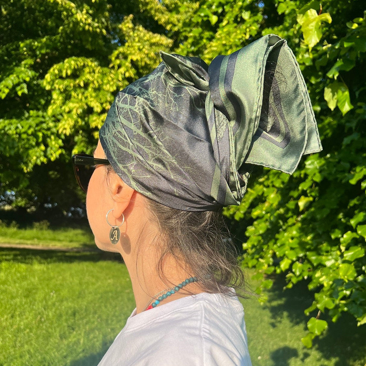 Person wearing a green patterned headscarf /silk scarf in a park setting.