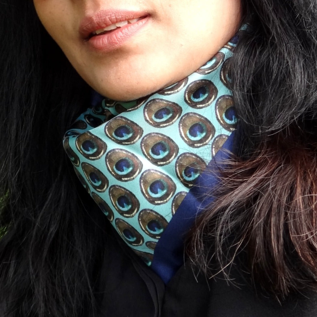 Woman wearing a peacock feather print silk scarf in shades of turquoise blue.
