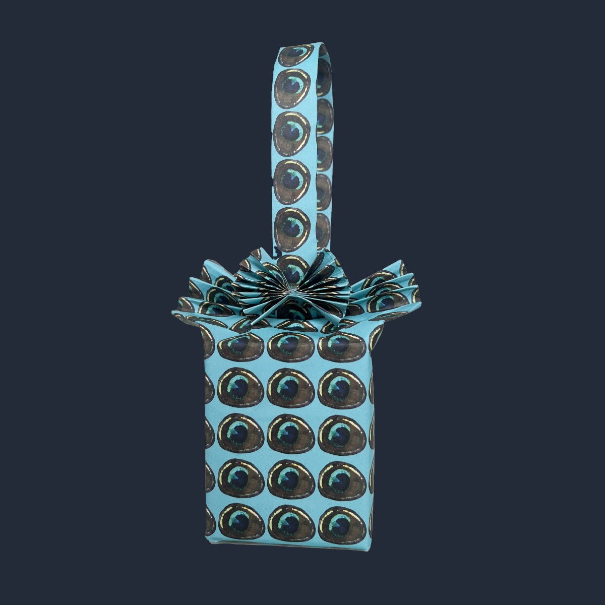 Gift artistically wrapped as a bag in Rumi London eco-friendly wrapping paper in repeat peacock feather print on a blue base. 
