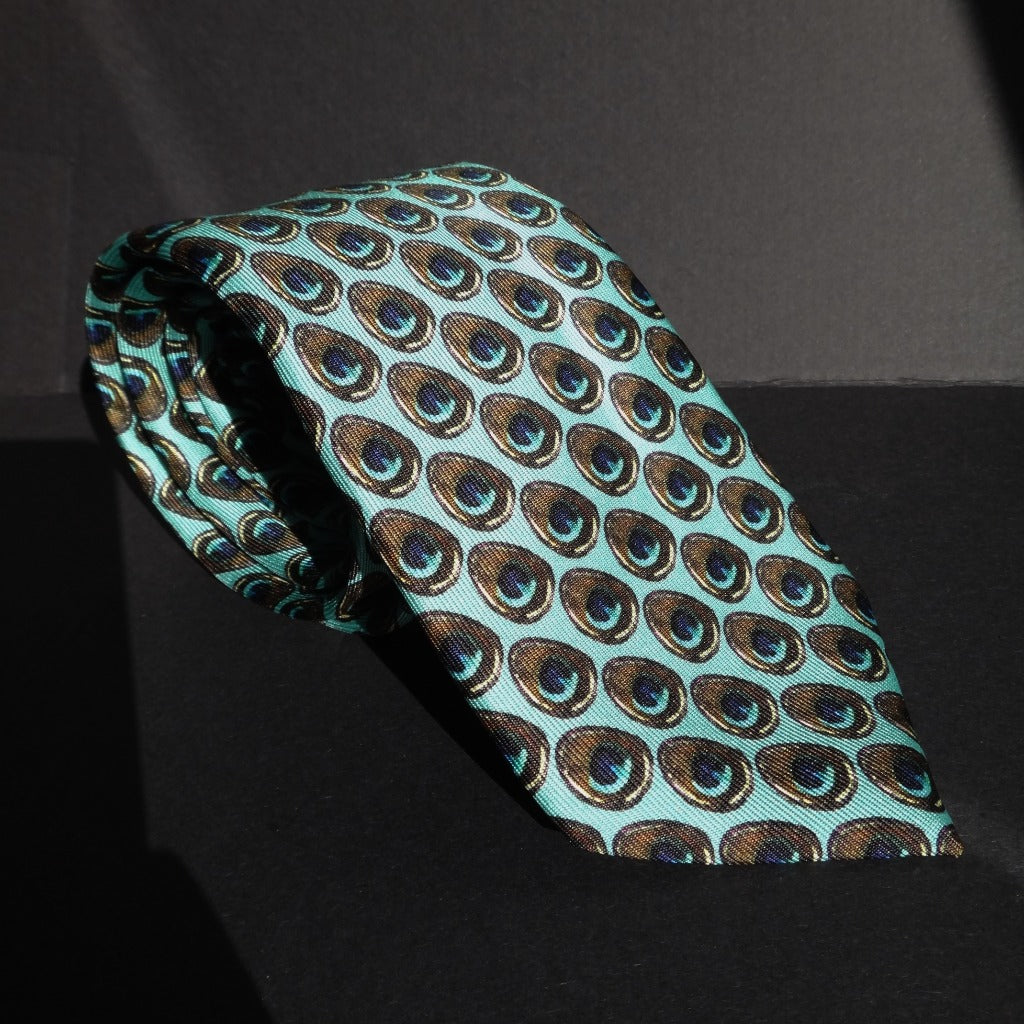 Pure Silk Peacock Feather Motif Tie rolled and placed on a black base.