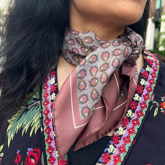 Woman wearing a silk scarf with a repeat pattern featuring conches on a brown base.