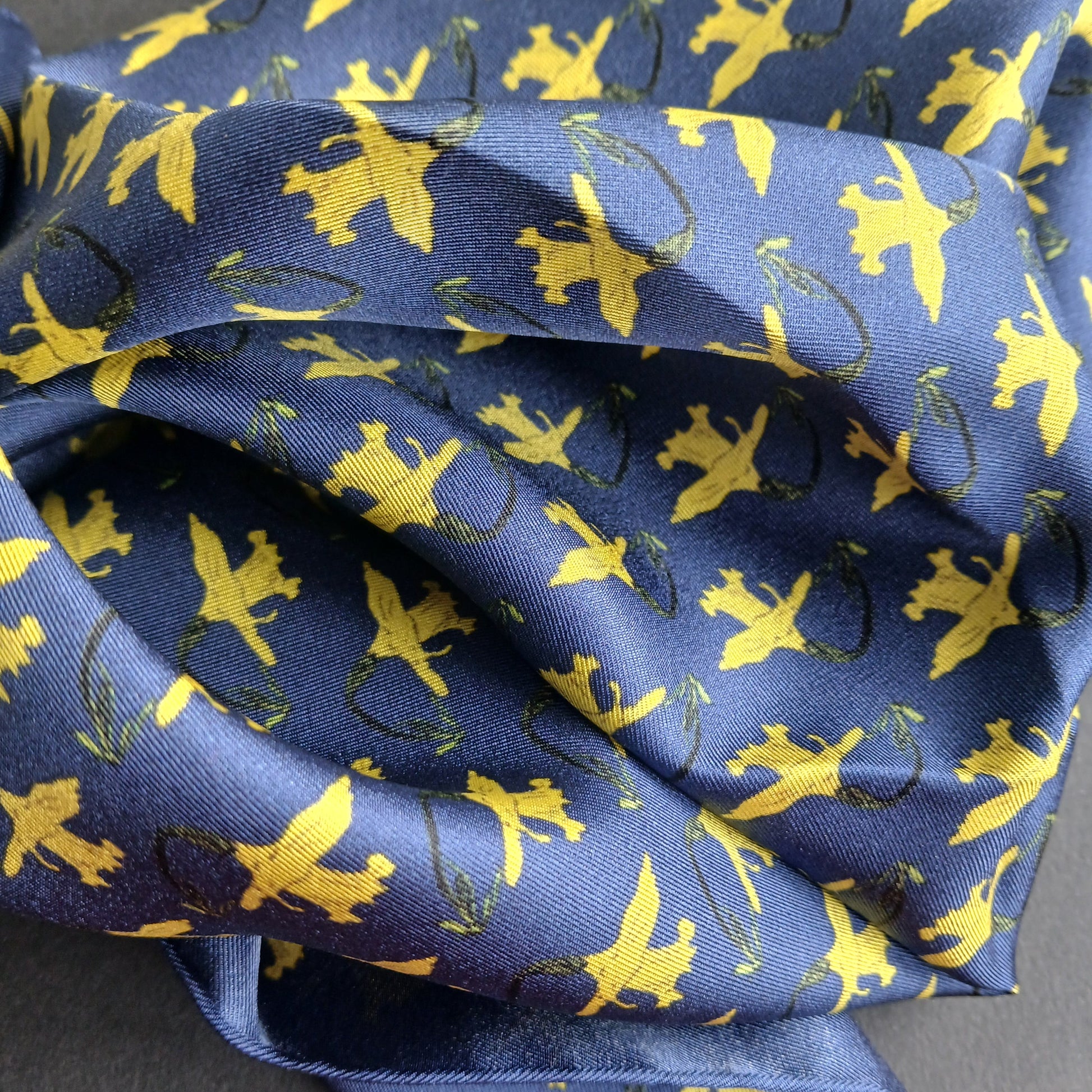 A navy blue silk pocket square with a repeating yellow daffodils pattern on a blue base.