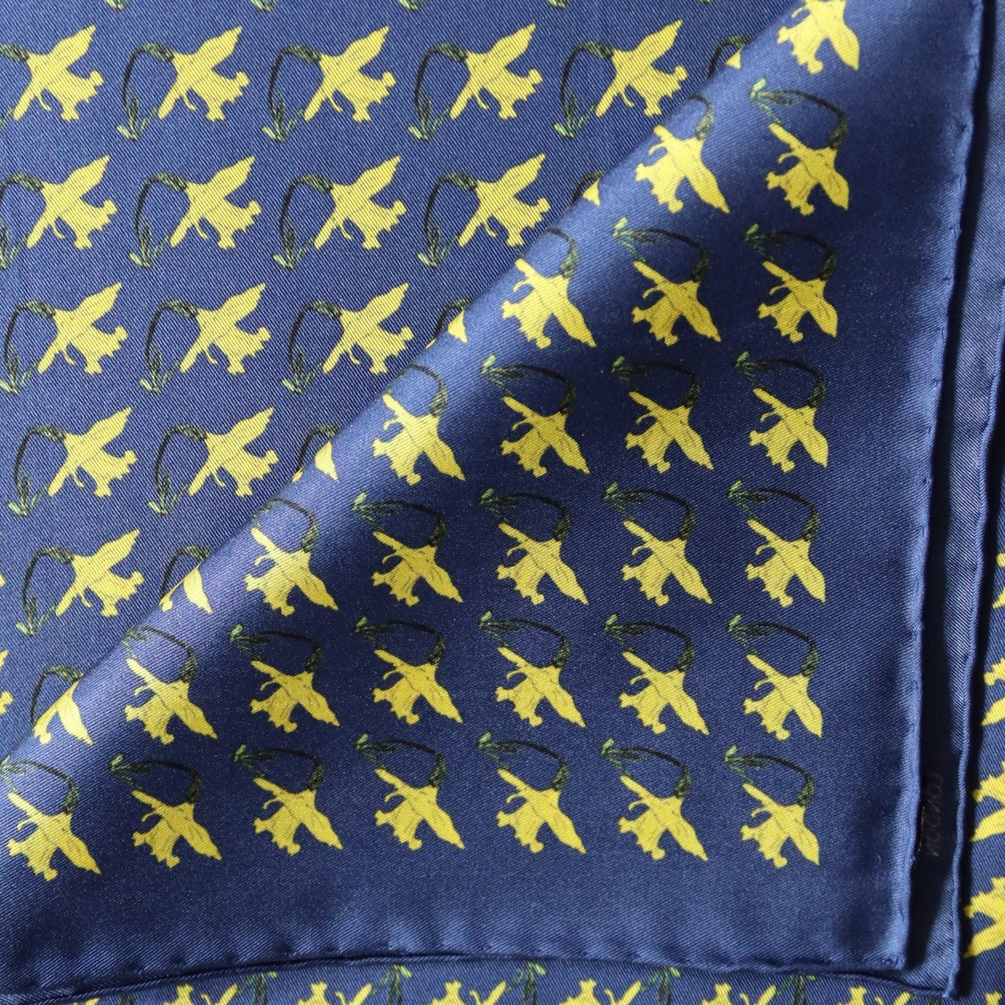 A navy blue silk pocket square with a repeating daffodils floral pattern.