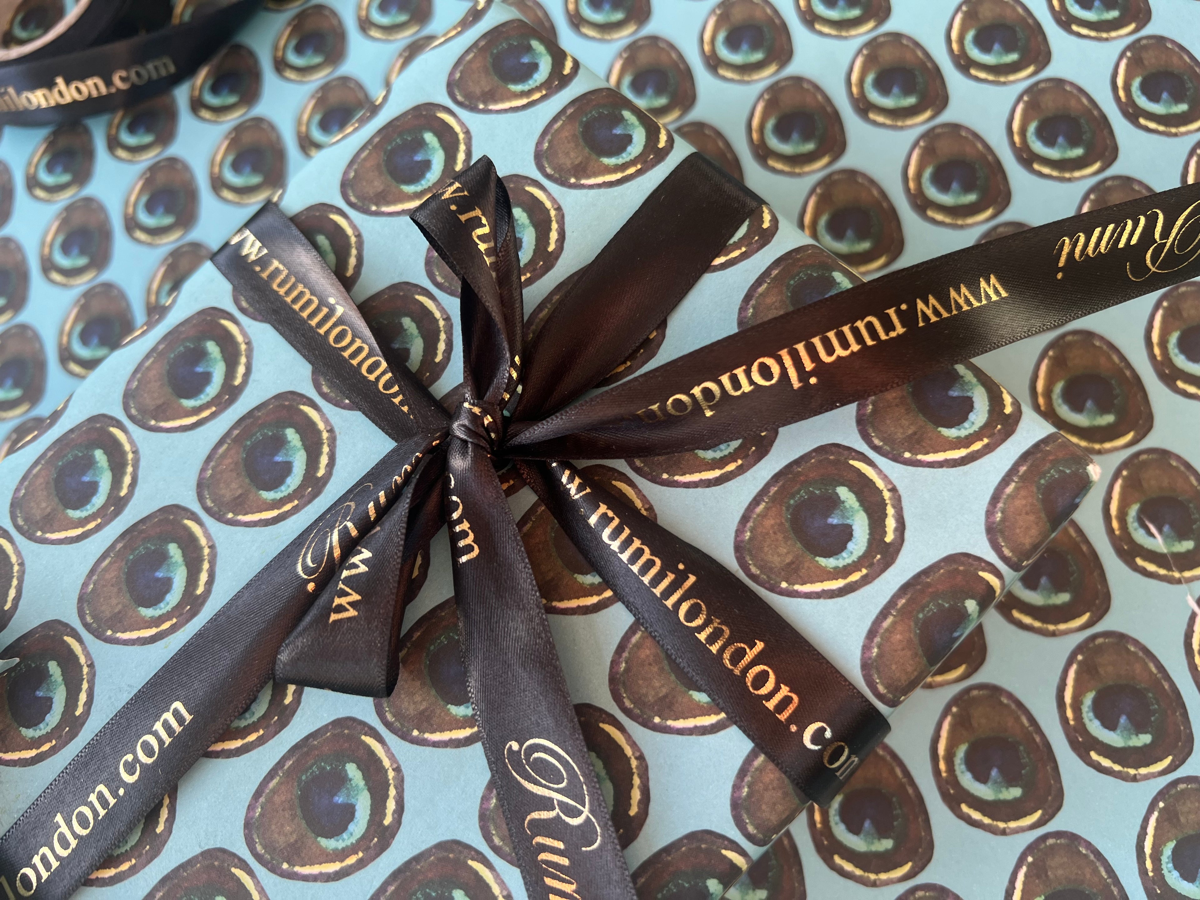 Rumi London Eco-friendly Wrapping Paper in repeat peacock feather pattern on a blue base.