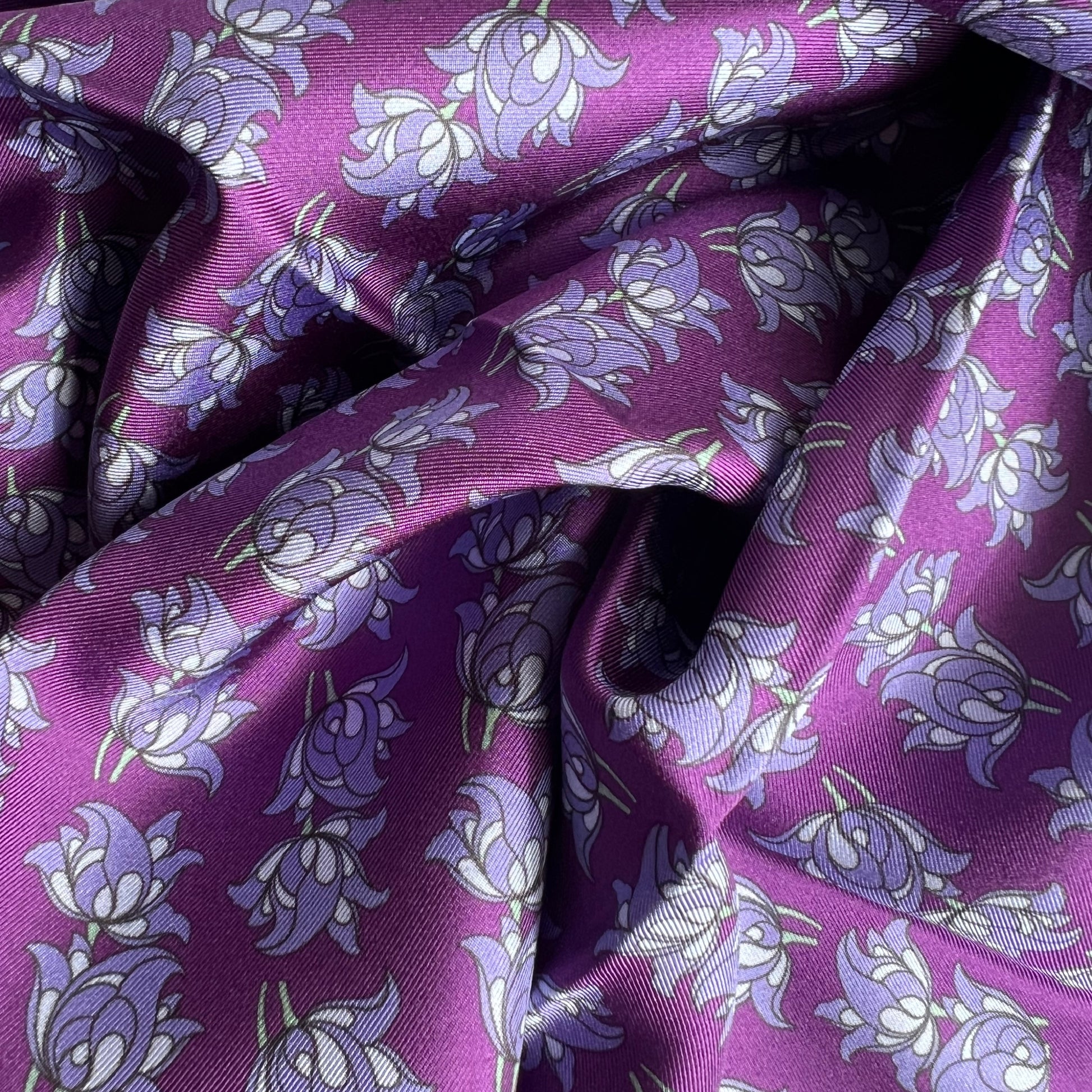 Close-up of purple floral silk twill silk scarf with floral motif repeat pattern on a purple base.