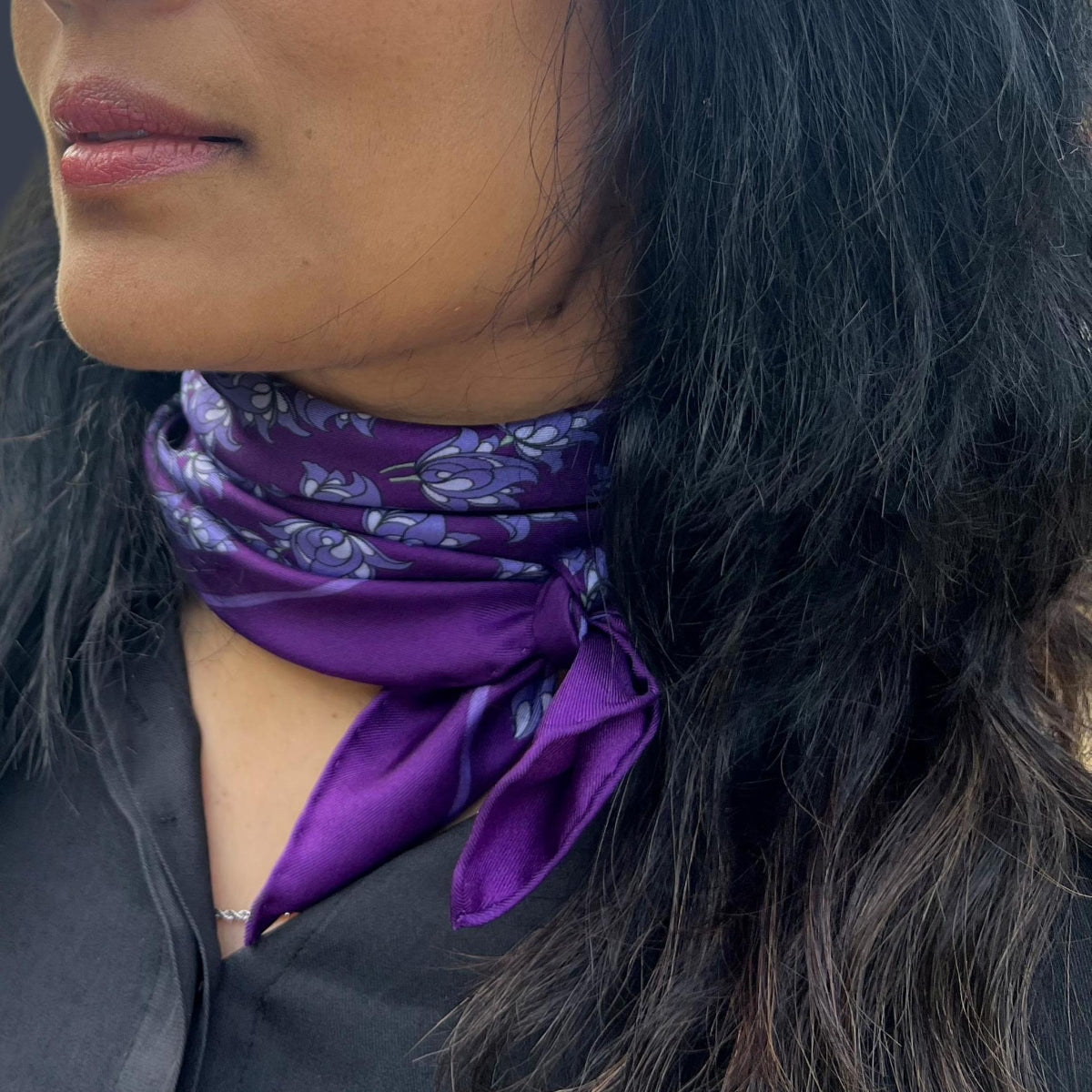 Woman wearing a purple floral motif silk twill scarf around her neck