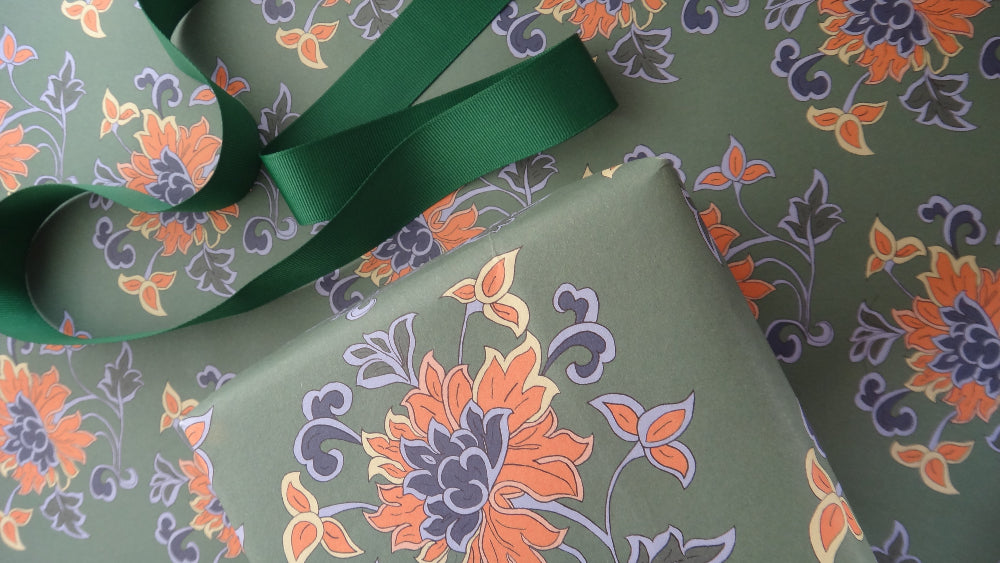 Floral-patterned wrapping paper with a green ribbon on top, featuring colourful flowers on a green base.