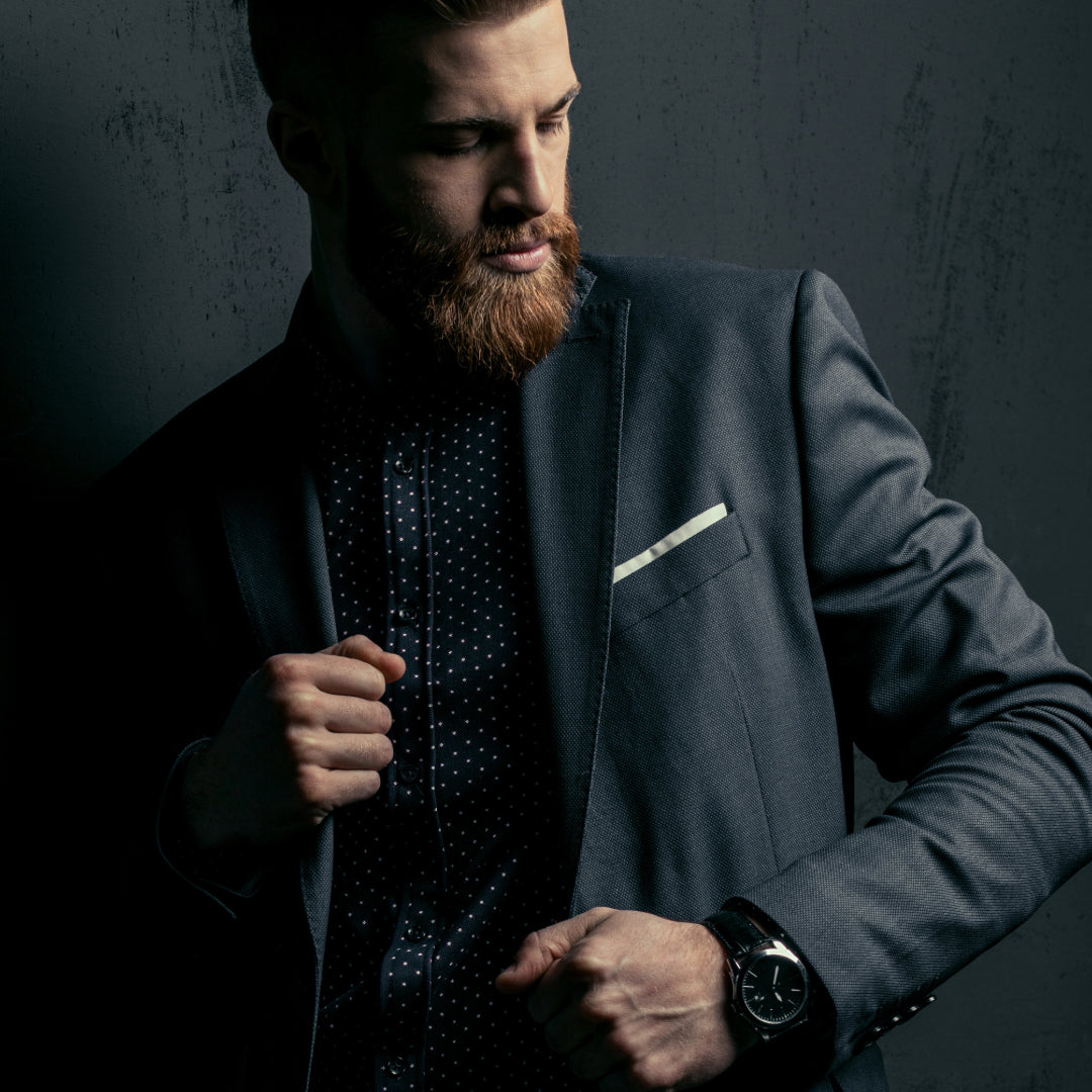 Man in a suit with a beard against a dark background earing pocket square
