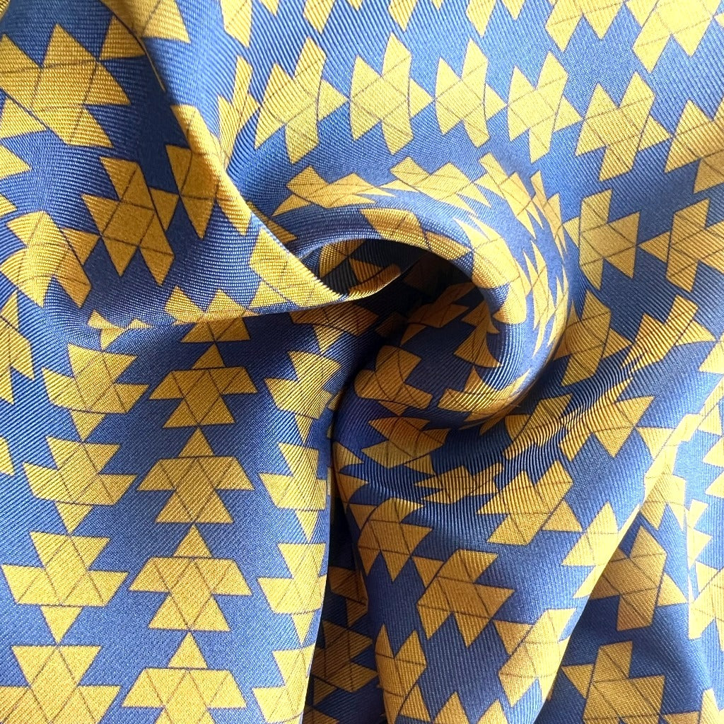 Close-up of square silk scarf with blue and yellow motifs on a lue base.