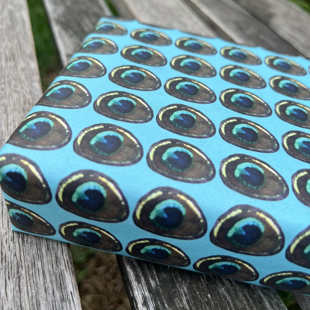 Gift wrapped in Rumi London eco-friendly wrapping paper in repeat peacock feather print on a blue base.